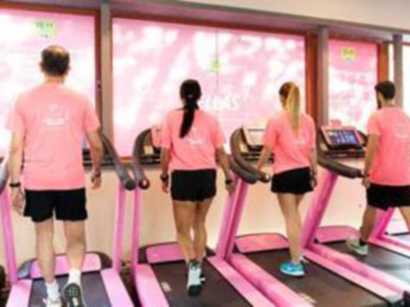 Gente haciendo ejercicio en máquinas de caminar en un gimnasio con paredes decoradas en tonos rosados y verdes.