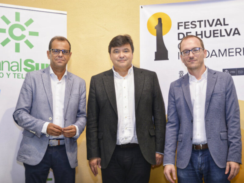 Tres hombres posan frente a dos banners, uno con el logo de Canal Sur y el otro con el Festival de Música de Huelva.