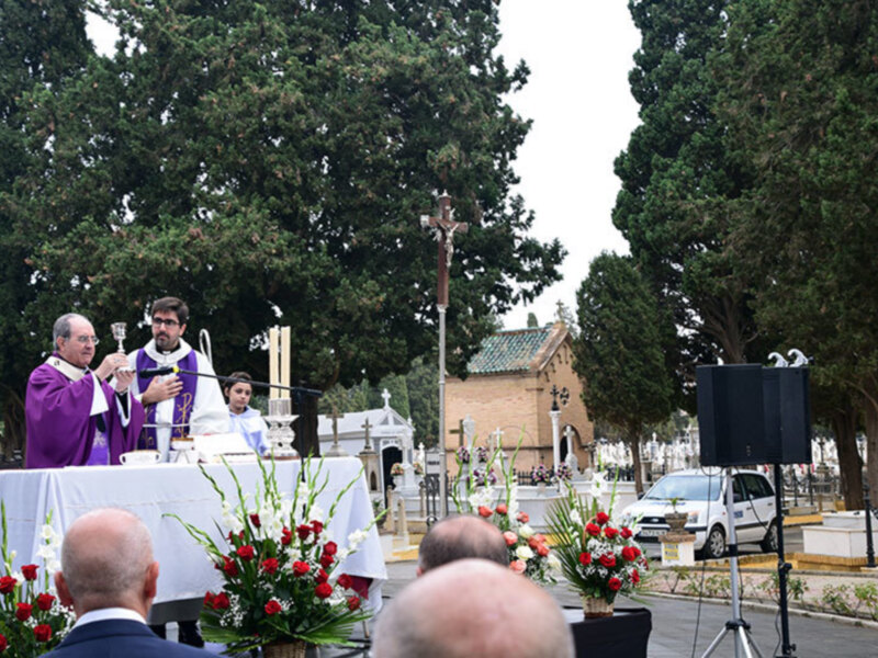Celebración religiosa en un cementerio con un sacerdote oficiando una misa.
