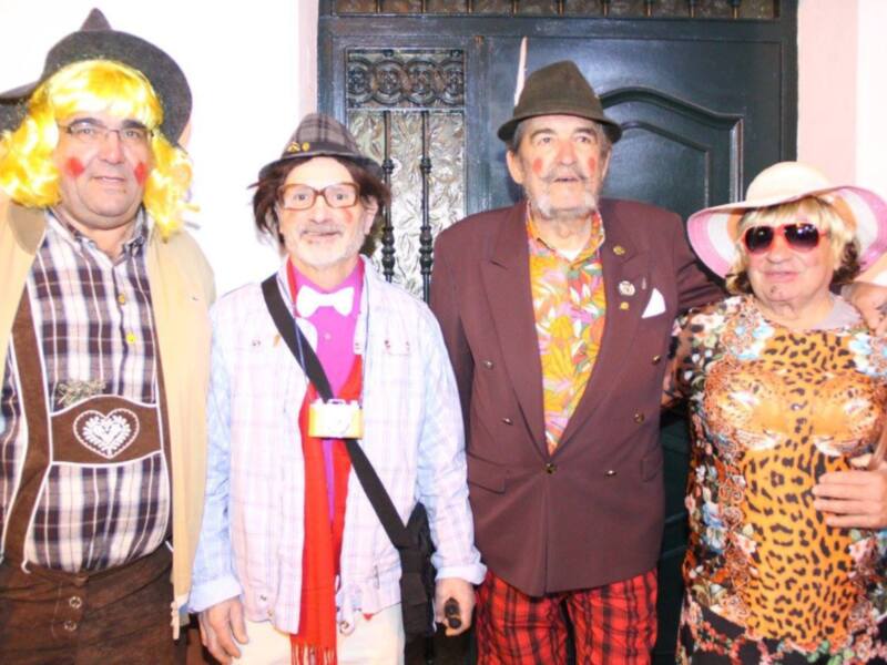 Personas vestidas con trajes coloridos y accesorios divertidos posan juntas en un evento festivo.