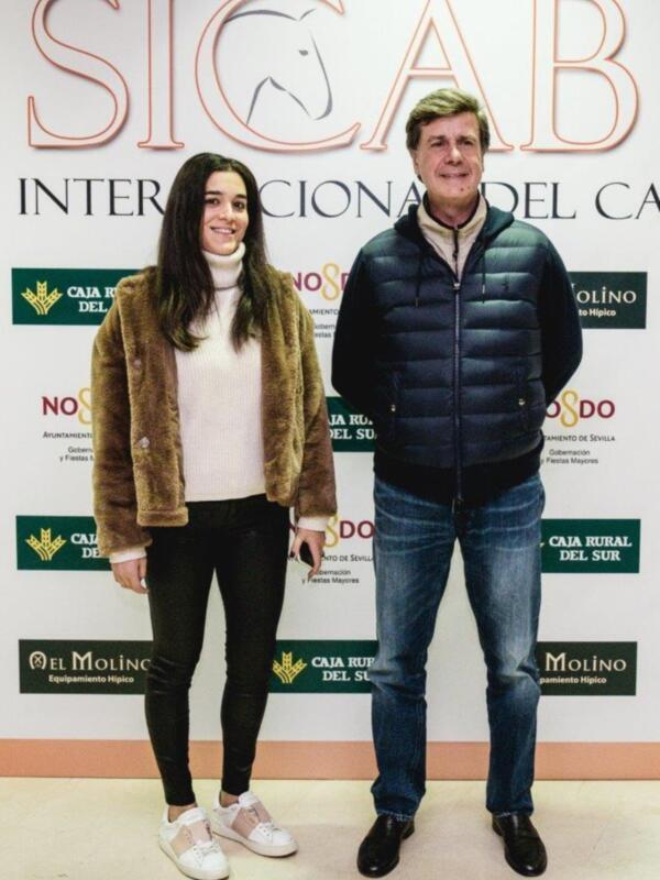 Dos personas posando en una foto con un fondo que incluye el logo de SICAB y otros patrocinadores. La imagen es de una exposición o evento relacionado con el hipismo en Sevilla.
