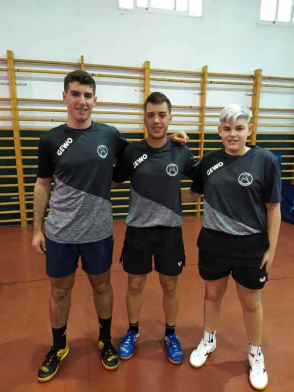 Tres jóvenes atletas posando juntos en un gimnasio, vestidos con uniformes deportivos y zapatillas de tenis.