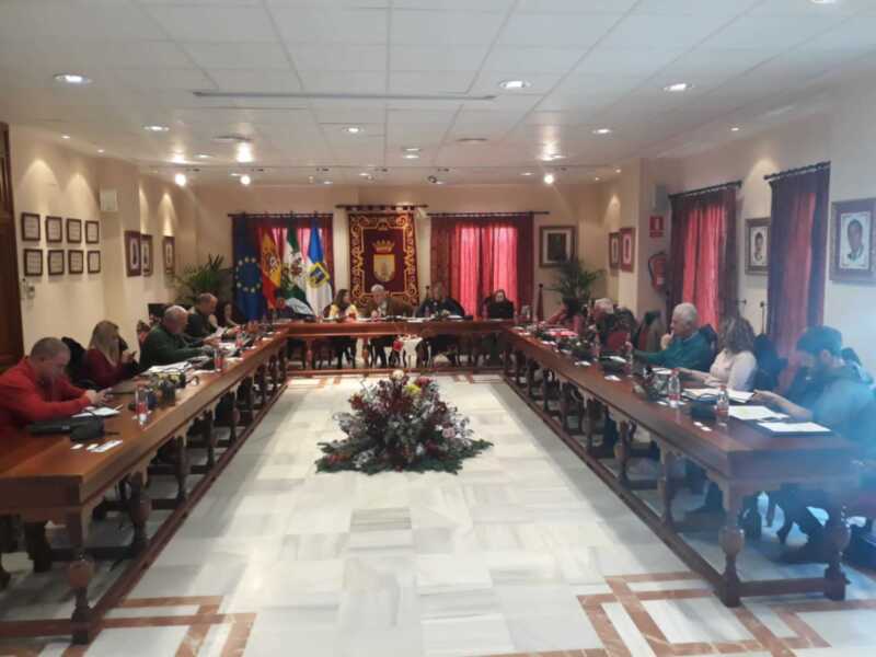 Reunión de consejo municipal en una sala con banderas y decoración formal.