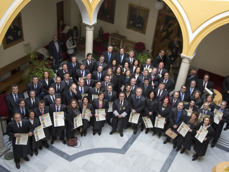 Celebración de una ceremonia con profesionales en trajes formales y certificados en mano, en un patio clásico con arcos y decoración navideña.