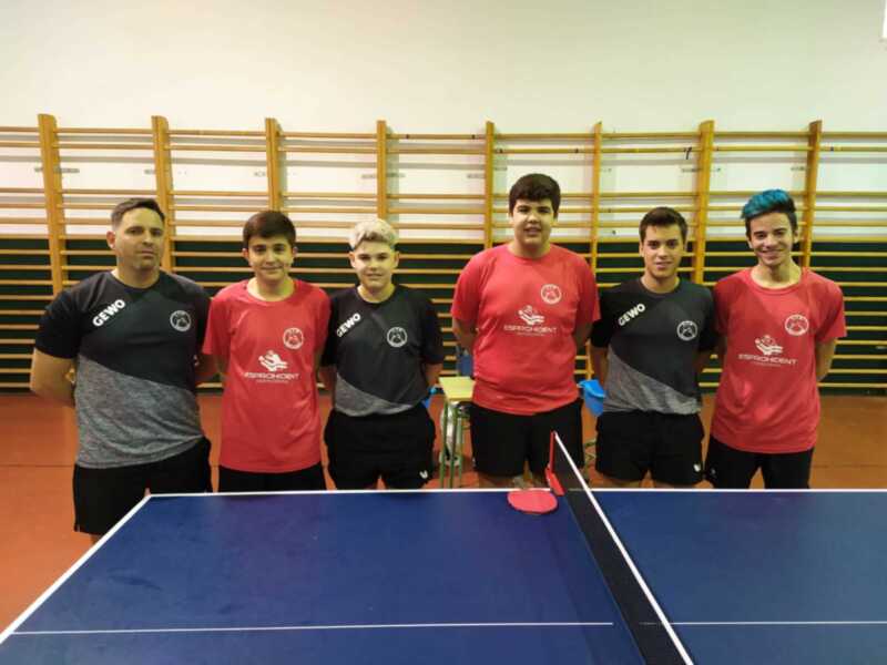 Equipo de tenis de mesa con entrenador en una cancha deportiva.