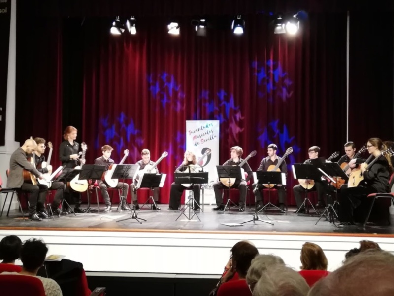 Concierto de guitarra en el Teatro Cajasol, Sevilla, con un grupo de músicos interpretando en un escenario bien iluminado.