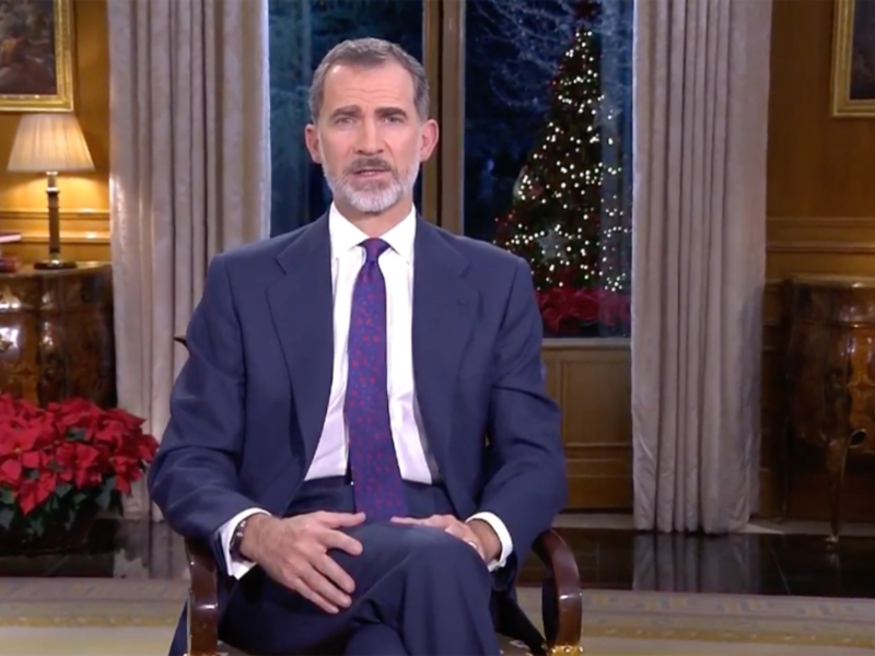 El rey Felipe VI de España durante su discurso navideño, sentado en un sillón frente a una decoración navideña con un árbol de navidad y una figura religiosa en el fondo.