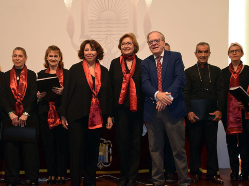 Gruppo di persone in abiti formali con sciarpe rosse, posano per una foto ufficiale in un ambiente formale.