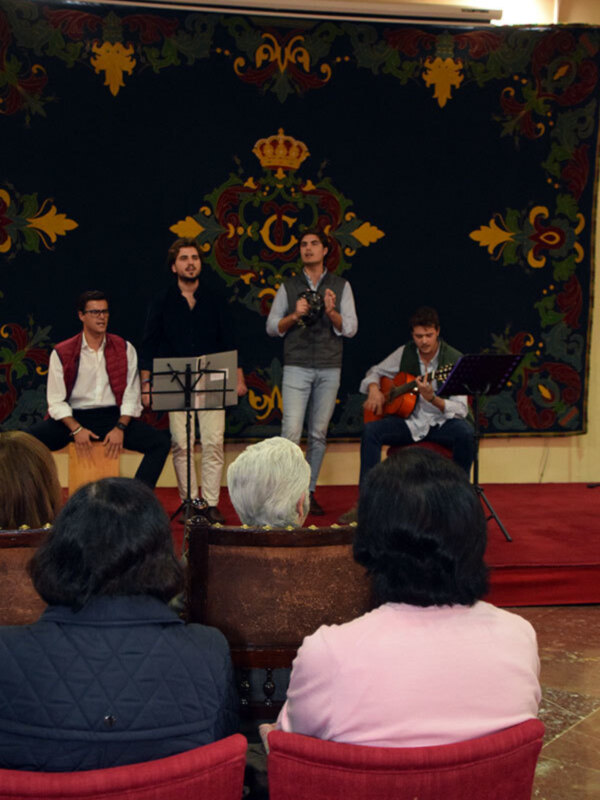 Concierto de música clásica en un escenario decorado con ornamentos florales y coronas, con músicos interpretando en un ambiente acogedor.