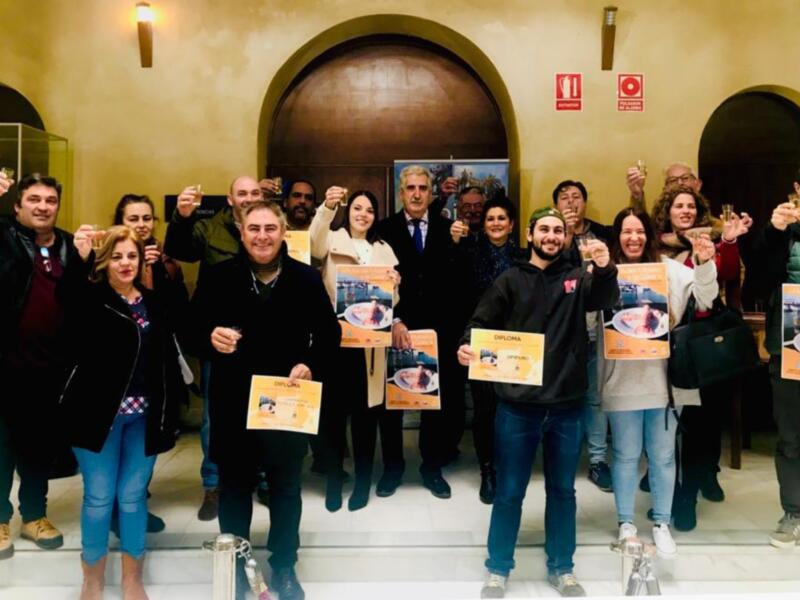 Una celebración con un grupo de personas sosteniendo diplomas y brindando con copas de vino, posiblemente en un evento de certificación o graduación.
