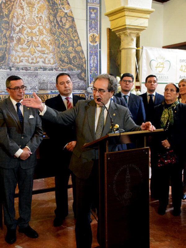 Persona hablando en un evento formal en un salón decorado con azulejos de Talavera.
