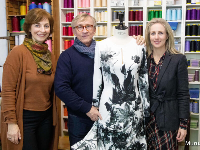 Tres personas posan junto a un maniquí con un vestido floral en una tienda de telas y hilo.