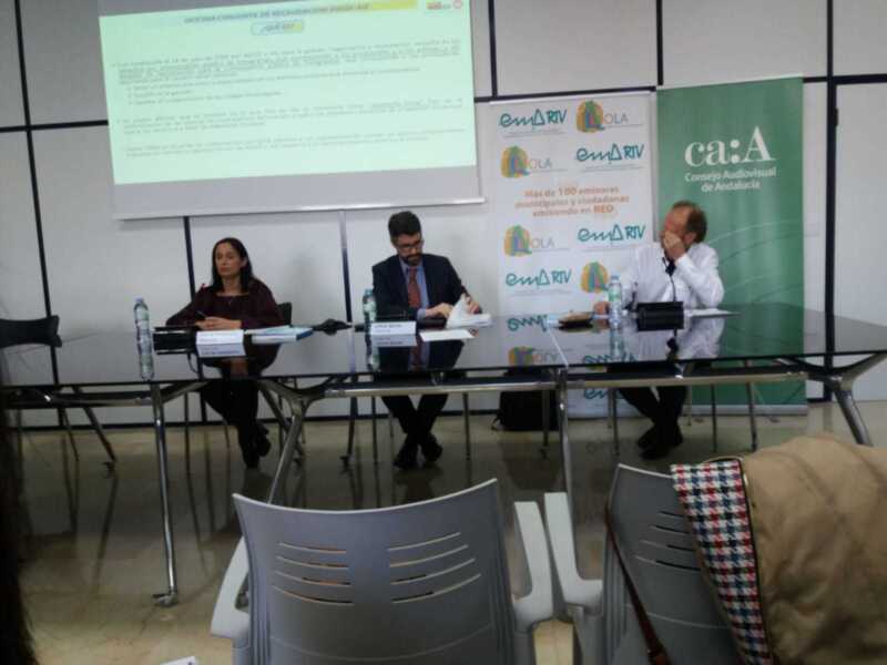 Reunión informativa del Consejo Audiovisual de Andalucía en una sala de conferencias con paneles y carteles informativos.