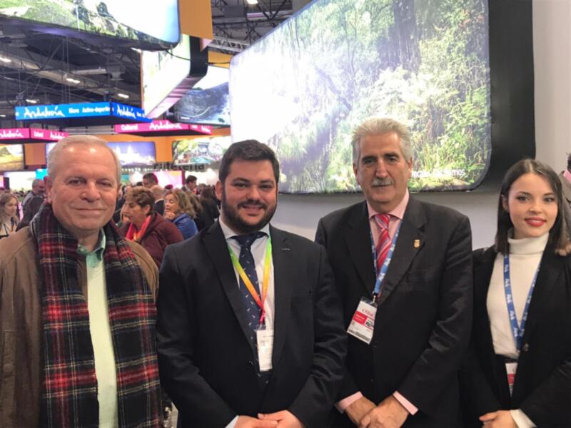 Expositores y visitantes en una feria turística, con un fondo de pantalla de paisaje natural.