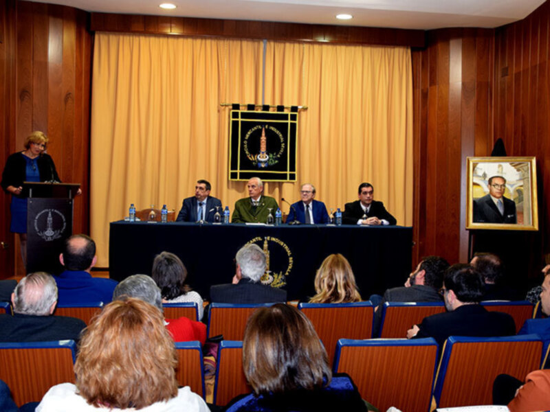 Una conferencia de prensa en un auditorio con una mesa de conferencia y varios oradores, en el fondo se puede ver una bandera con un símbolo religioso y una foto de un líder político enmarcada.