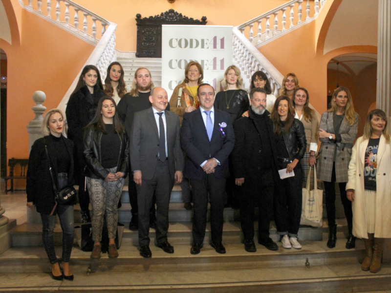 Grupo de personas posando para una foto en un evento de CODE41 en un salón con escalera y decoración clásica.