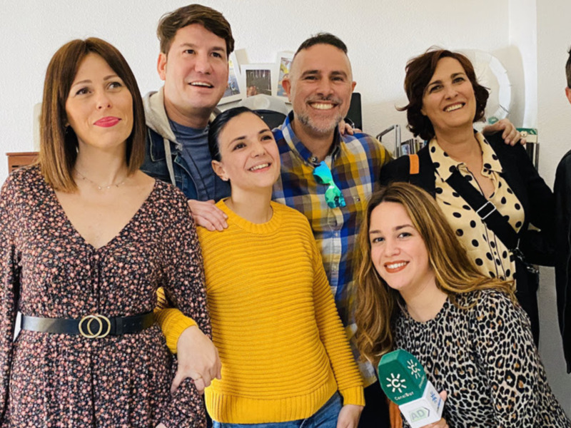 Un grupo de amigos sonríe juntos en un ambiente acogedor, rodeados de detalles personales en la pared.
