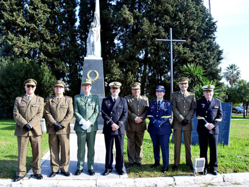 Oficiales militares en ceremonia frente a un monumento conmemorativo en un entorno verde.