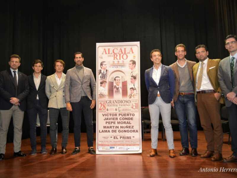 Grupo de hombres posando en el escenario junto a un cartel promocional de un festival taurino en Alcalá de Henares.