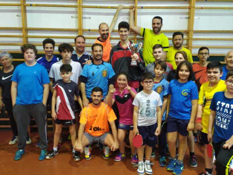 Equipo de tenis de mesa celebrando con trofeo en una cancha deportiva.