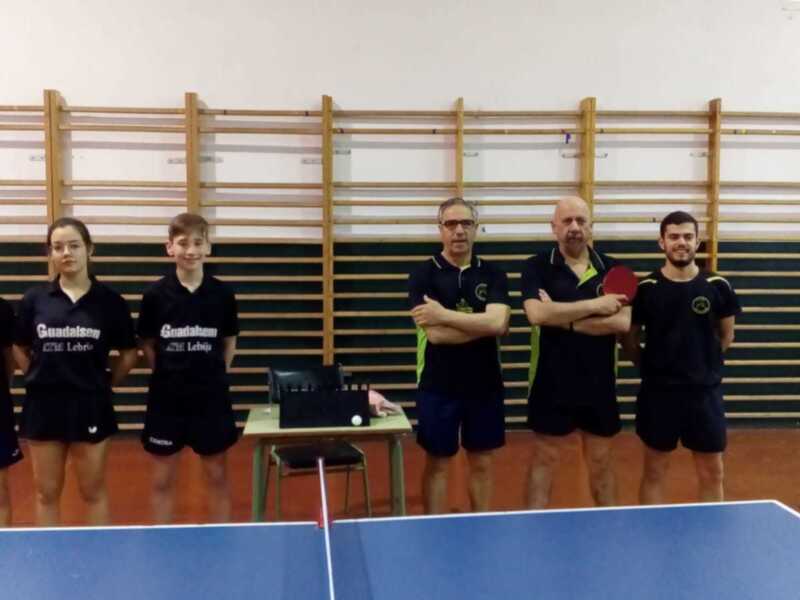Equipo de tenis de mesa con entrenadores y jugadores en una sala de deportes.