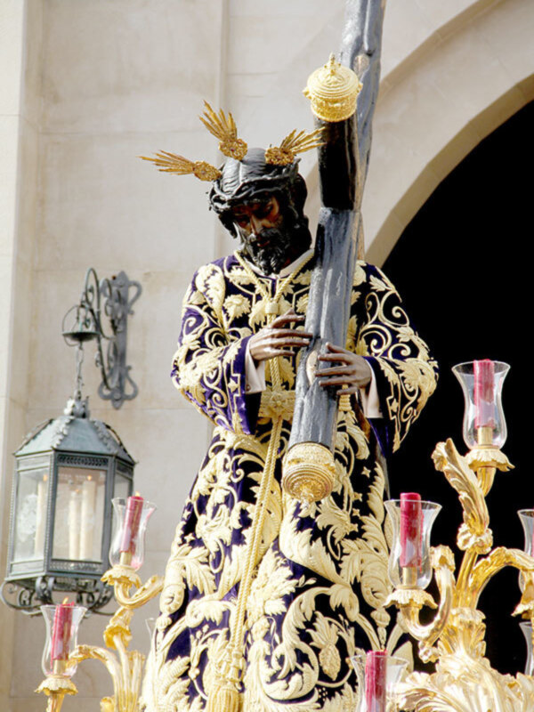Figura religiosa procesional con traje ornado y cruz, en un entorno de iglesia.