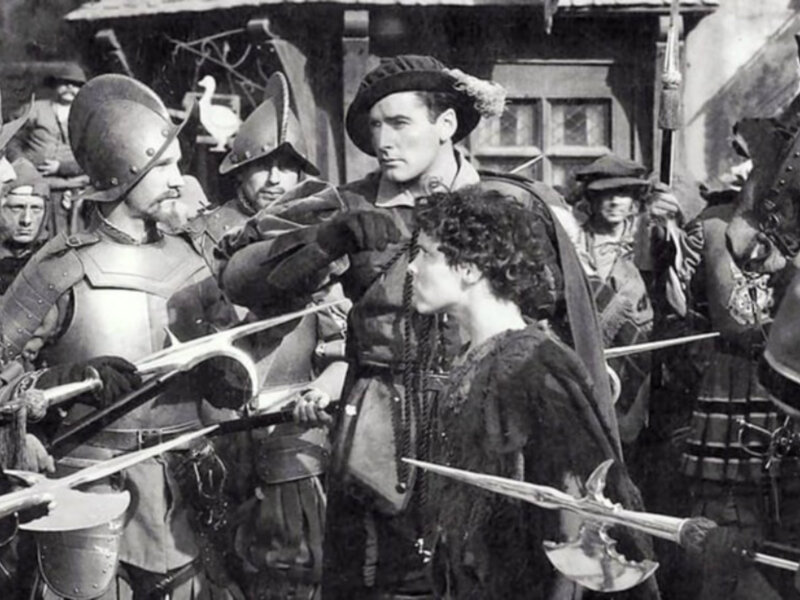 Escena histórica con personajes vestidos con armaduras y trajes medievales, posiblemente de una película o escenificación teatral.