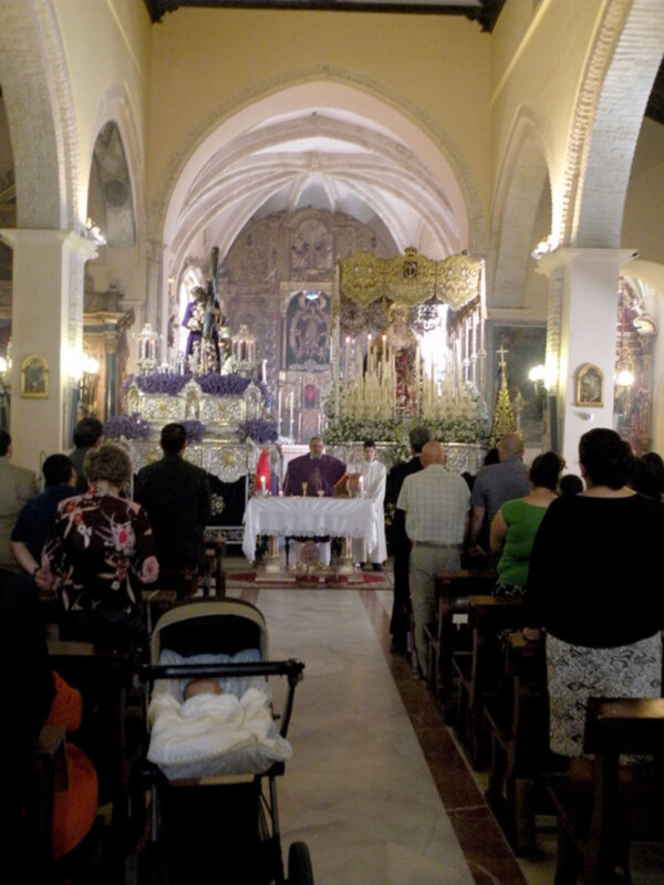 Interior de una iglesia durante una misa, con altares ornamentados y fieles en oración.