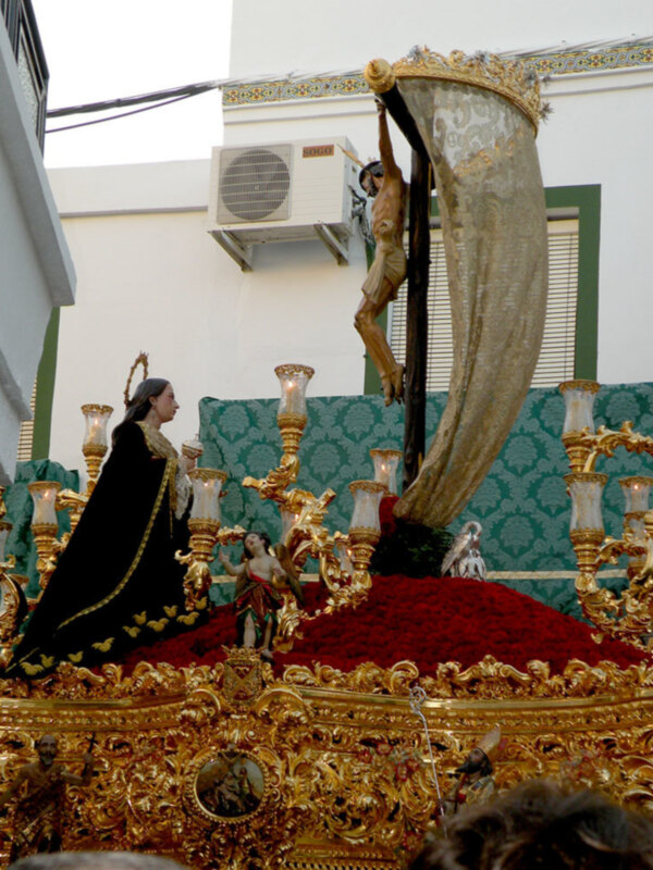 Estatua religiosa con detalles dorados y una corona en el cielo, con una persona en el fondo.