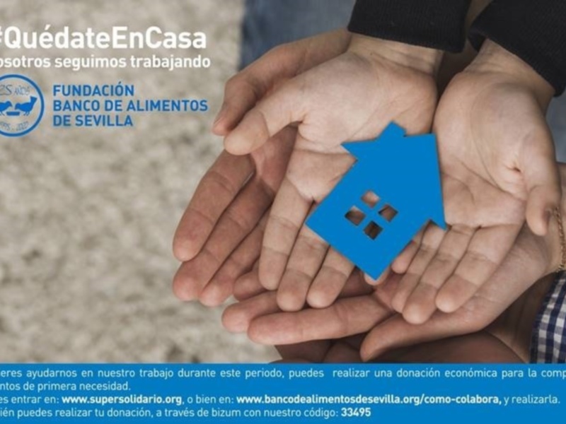 Manos sosteniendo una casa azul, con el texto #QuédateEnCasa y información sobre la Fundación Banco de Alimentos de Sevilla para donaciones de alimentos de primera necesidad.