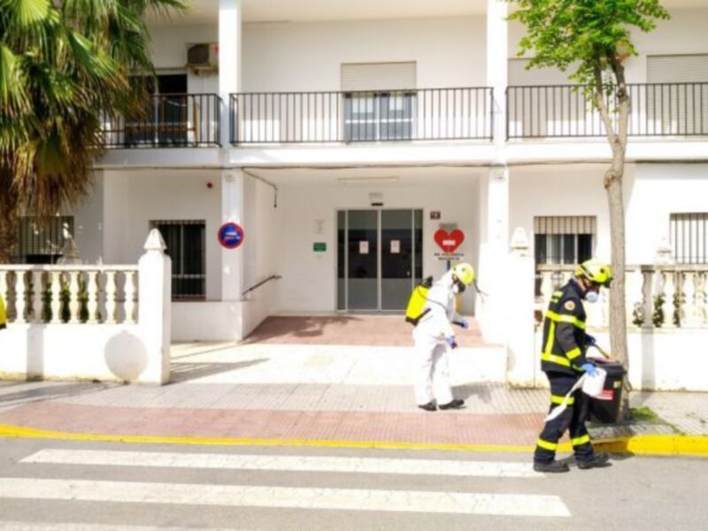 Equipo de desinfección y bomberos trabajando frente a un edificio blanco.