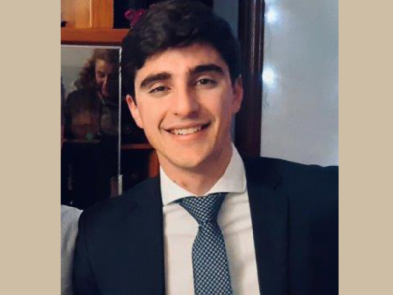 Persona joven en traje y corbata sonriendo en un entorno interior.