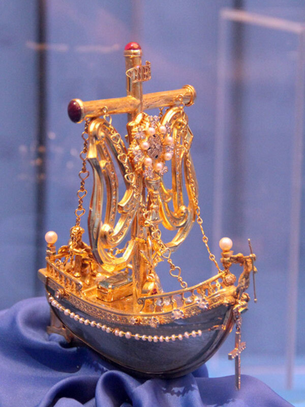 Miniatura de barco de oro con detalles ornamentales y perlas, expuesta en un museo.