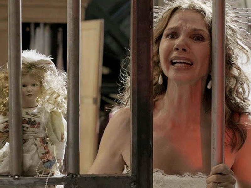 Una mujer en vestido de novia y una muñeca detrás de rejas en una escena de terror.