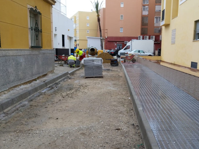 Trabajadores en una obra de construcción en una calle urbana, con maquinaria y materiales de construcción alrededor.