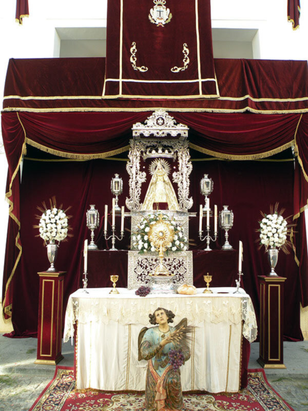 Altar con estandarte y estatua de la Virgen María, ornado con flores y candelabros, en un entorno religioso.