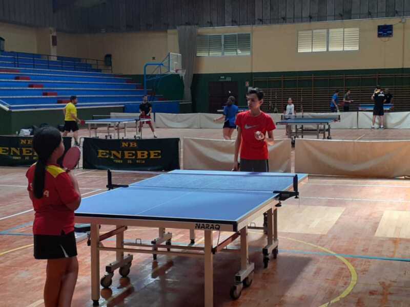 Jugadores de tenis de mesa en acción en un gimnasio deportivo.
