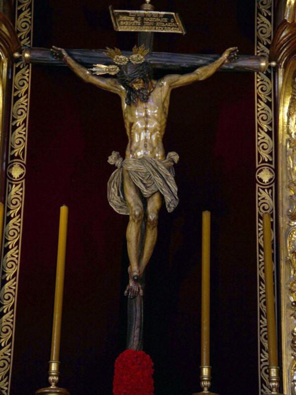 Cristo en la cruz con candelabros y adorno rojo en un entorno religioso.