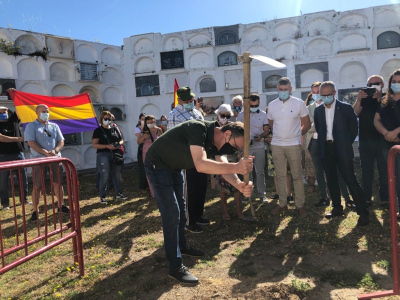 Ceremonia con bandera LGTBI en cementerio con personas con máscaras y un hombre excavando