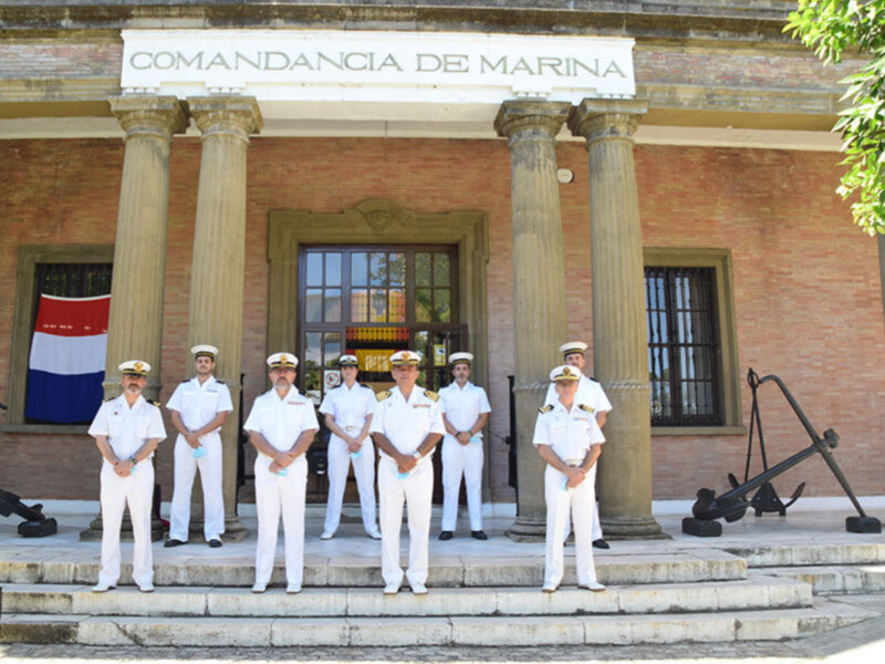 Fotografía de oficiales de la Armada en uniforme frente a la Comandancia de Marina, con un ancla en el fondo.