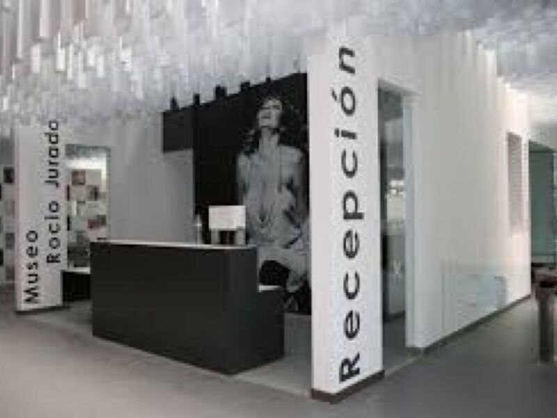 Recepción del Museo Rocío Jurado, moderno y minimalista con recepcionista y cartelera informativa.