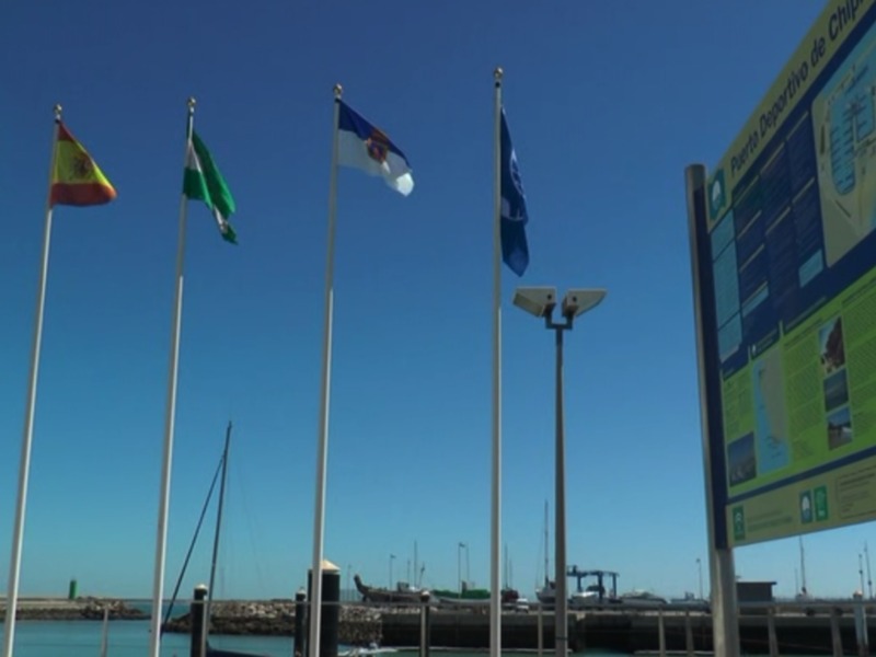 Vista del Puerto Deportivo de Chipiona con banderas y paneles informativos al sol.