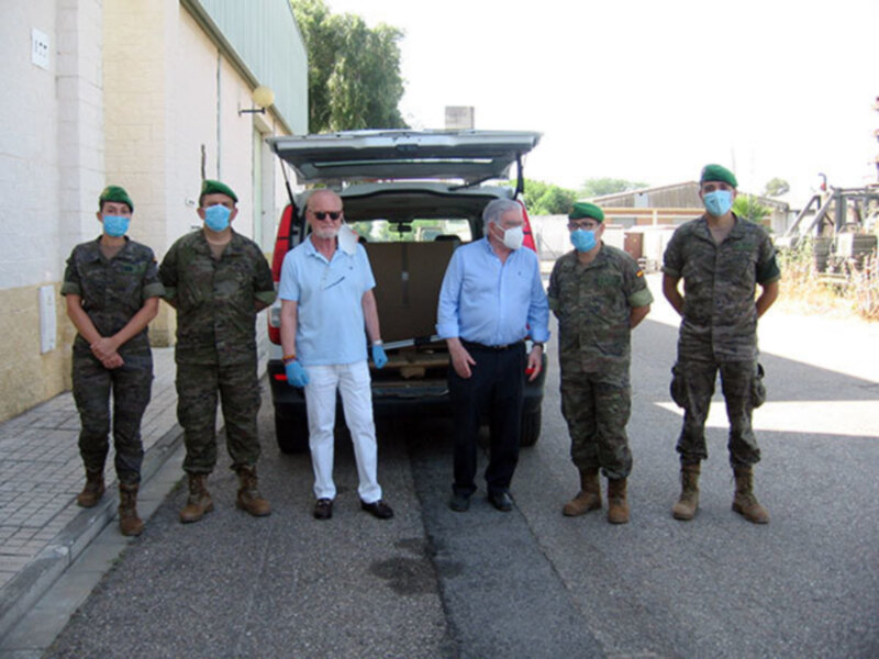 Un grupo de personas, incluyendo militares, posando frente a un vehículo. Todos están vestidos con uniformes militares y algunos llevan máscaras faciales. La escena parece ser en un entorno urbano, con edificios y vegetación al fondo.