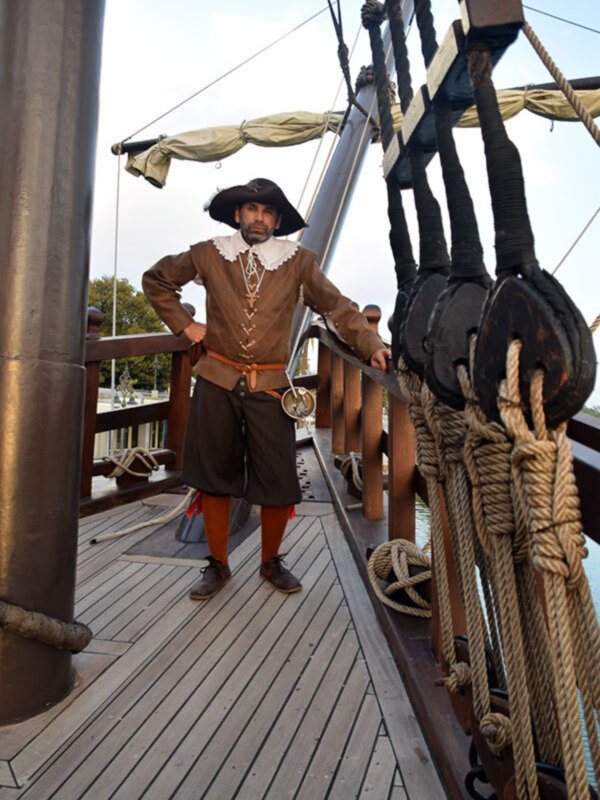 Imaginación histórica: Un hombre vestido con traje colonial posa en la cubierta de un barco antiguo, con detalles como cuerdas, palos y una vela visible en el fondo.