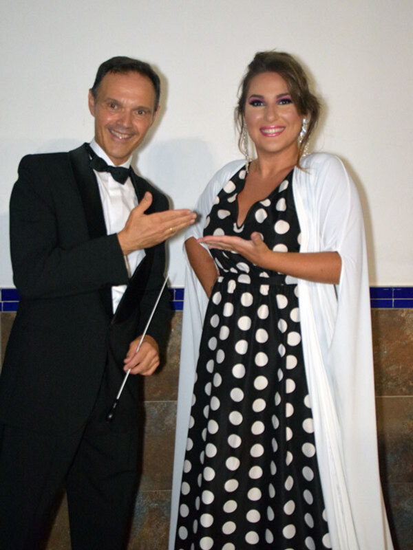 Elegante pareja en traje y vestido de lunares, posando frente a una pared de azulejos azules.