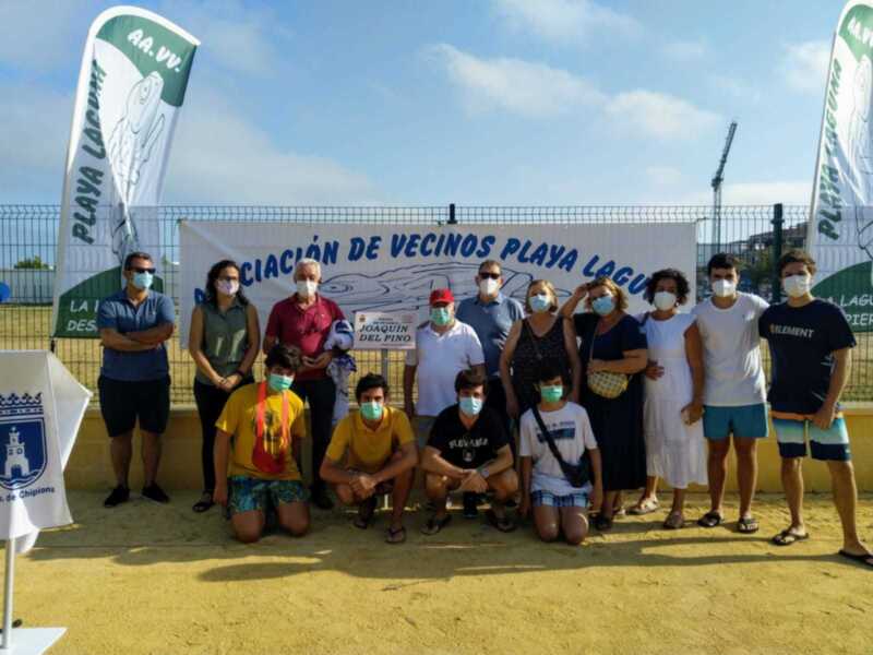 Gruppo di persone con mascherine in posa davanti a una bandiera con il logo dell'associazione "Asociación de Vecinos Playa Lagunilla".