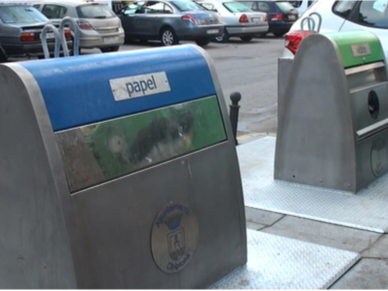 Contenedores de reciclaje para papel y otros materiales en un aparcamiento urbano.