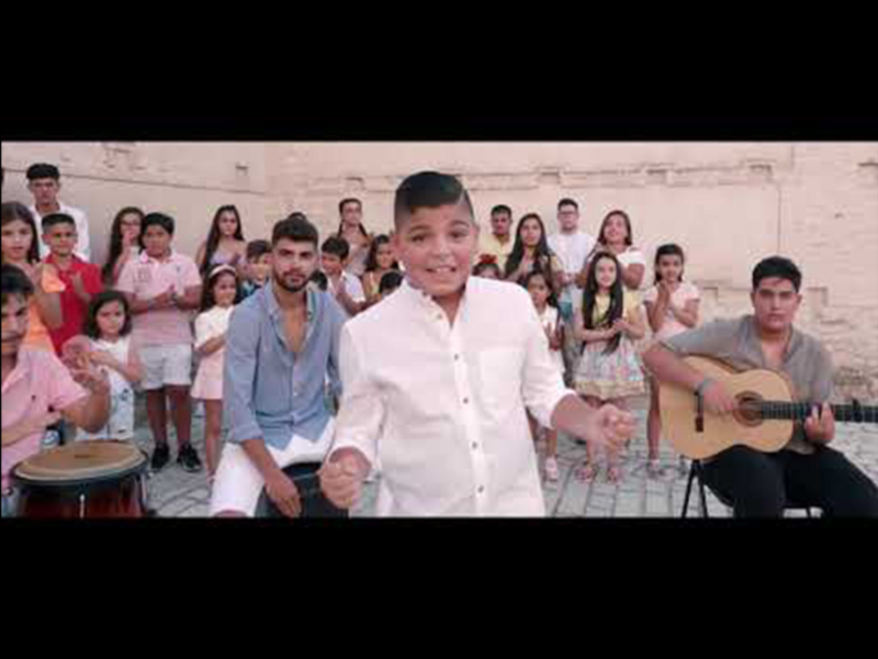 Joven cantante y músico tocando la guitarra, rodeado por un grupo de niños y jóvenes en un ambiente al aire libre.