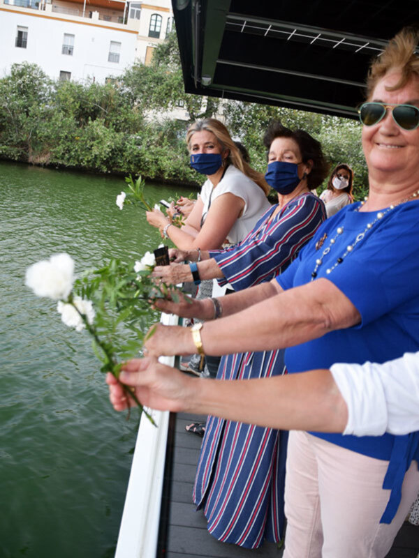 Grupo de personas en un barco, algunas de ellas llevan flores y máscaras, posiblemente durante una celebración o evento en el agua.