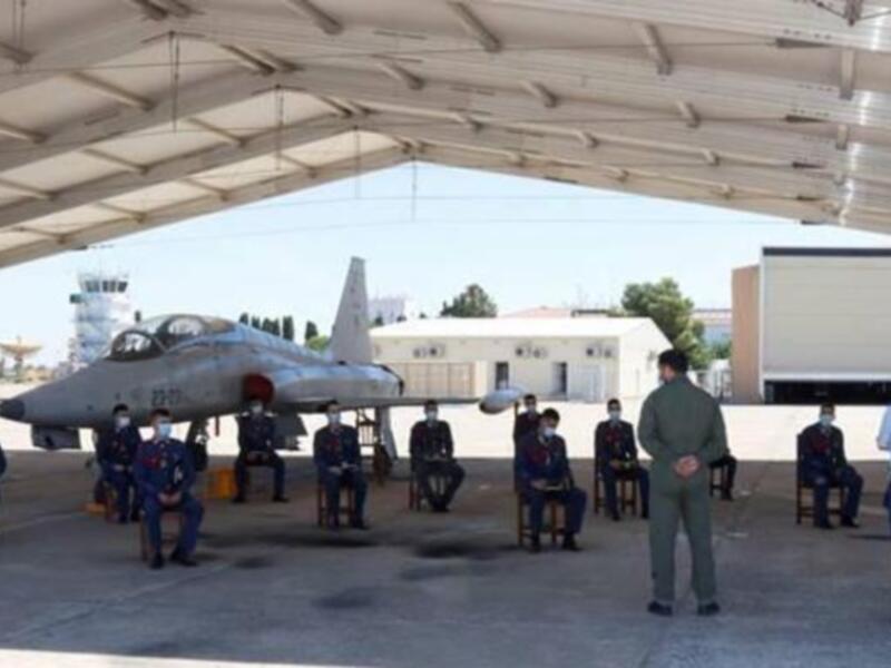 Personal militar en uniforme y máscaras, posando frente a un avión militar en una base aérea, durante una ceremonia de despedida o bienvenida.